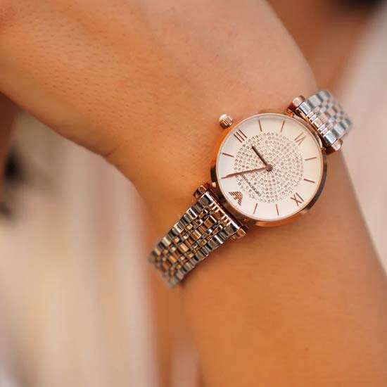 The Emporio Armani Gianni T-bar Analog Watch features a quartz movement, a white dial, a rose gold case color made of stainless steel, a round case shape with a size of 32 MM, and a case thickness of 8 MM.
